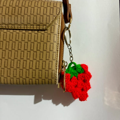Brown textured handbag with a red and green keychain on a white background