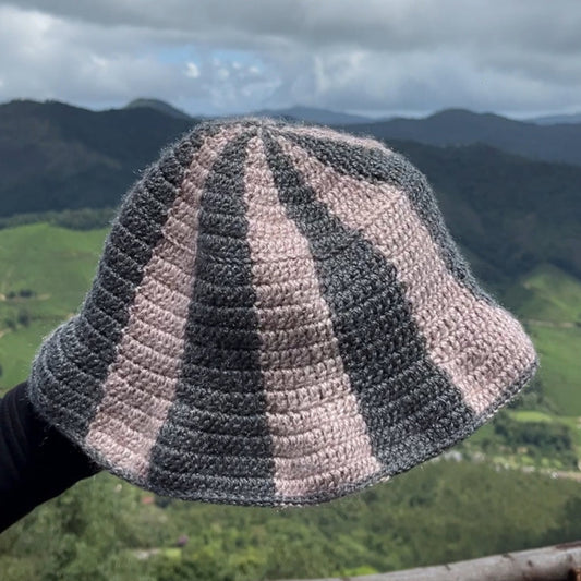 Crocheted hat with striped pattern held up against a scenic mountain backdrop