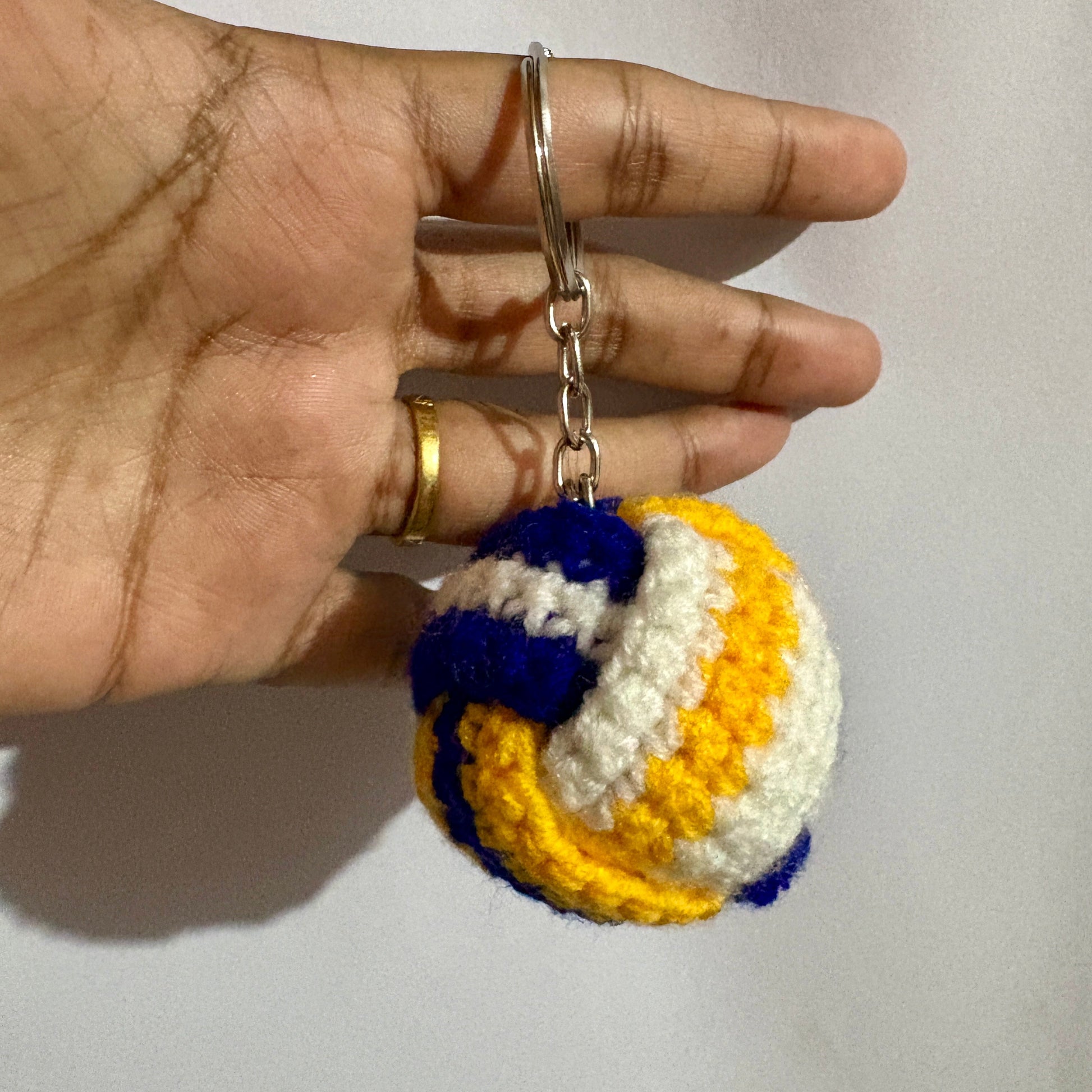 Hand holding a keychain with a colorful volleyball design against a plain background