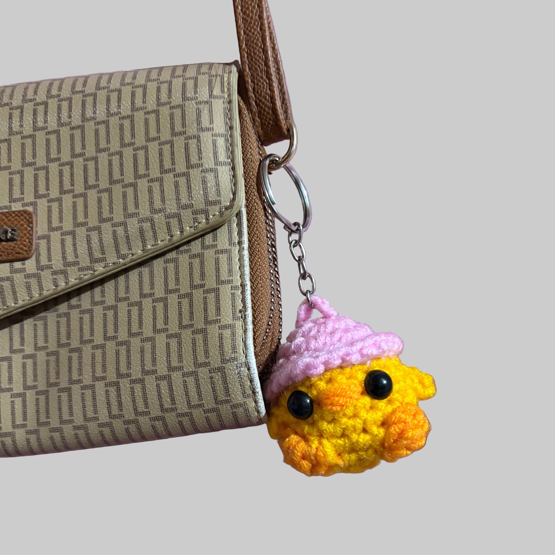 Small crochet chicken with hat keychain attached to a beige wallet on a light pink background